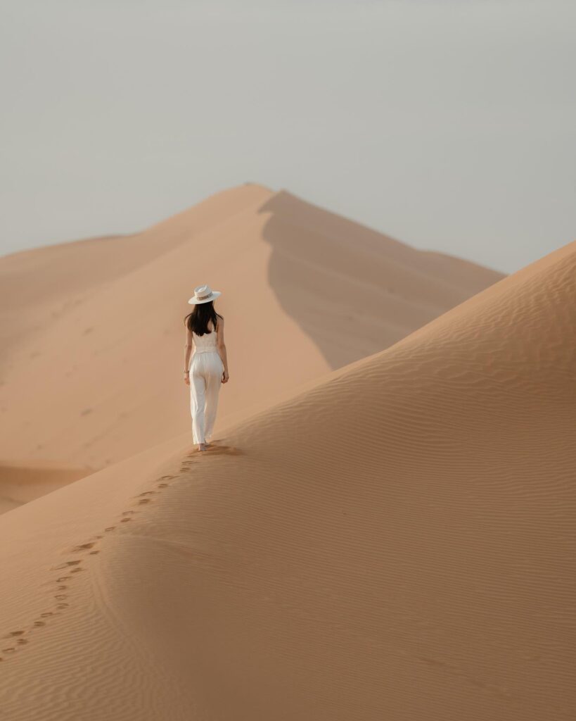A woman in white dress is walking on the sand dunes on Sahara desert.